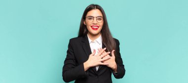 young pretty woman feeling romantic, happy and in love, smiling cheerfully and holding hands close to heart. business concept
