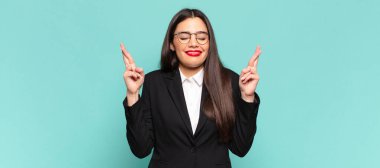 young pretty woman smiling and anxiously crossing both fingers, feeling worried and wishing or hoping for good luck. business concept