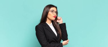 Yoğunlaşmış bakışları olan genç ve güzel bir kadın şüpheli bir ifadeyle yukarı ve yana bakıyor. iş kavramı