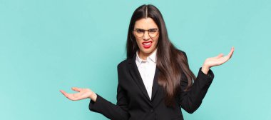 young pretty woman shrugging with a dumb, crazy, confused, puzzled expression, feeling annoyed and clueless. business concept