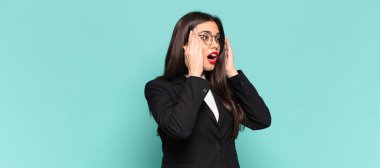 Genç, güzel bir kadın mutlu, heyecanlı ve şaşırmış hissediyor. İki eli de suratında yana bakıyor. iş kavramı