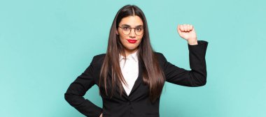 Genç ve güzel bir kadın ciddi, güçlü ve asi hissediyor, yumruğunu kaldırıyor, protesto ediyor ya da devrim için savaşıyor. iş kavramı