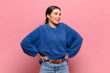 Genç, güzel bir kadın mutlu, neşeli ve kendinden emin görünüyor. Gururla gülümsüyor ve iki elini de kalçasında istiyor.