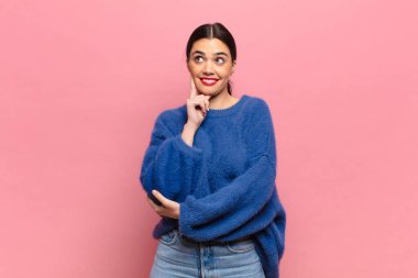 Genç ve güzel bir kadın mutlu bir şekilde gülümsüyor ve hayal kuruyor ya da şüphe ediyor.