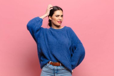 Genç, güzel bir kadın şaşkın ve kafası karışmış hissediyor, başını kaşıyor ve yan tarafa bakıyor.