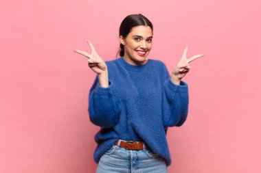 Genç ve güzel bir kadın gülümsüyor ve mutlu görünüyor, arkadaş canlısı ve memnun, işaret eden zafer ya da barış iki elle