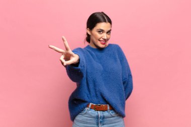 Genç ve güzel bir kadın gülümsüyor ve mutlu görünüyor, kaygısız ve pozitif, zafer ya da barış işareti yapıyor.