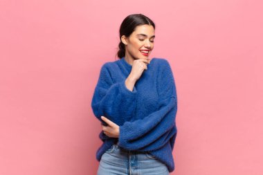 Genç, güzel bir kadın mutlu, kendinden emin bir ifadeyle gülümsüyor. Elleri çenesinde, merak ediyor ve yan tarafa bakıyor.