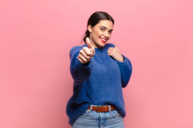 Genç, güzel bir kadın gururlu, tasasız, kendinden emin ve mutlu, başparmağıyla olumlu gülümsüyor.