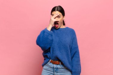 Genç, güzel bir kadın şok olmuş, korkmuş ya da korkmuş görünüyor. Yüzü elle kaplanmış ve parmaklarının arasından gizlice bakıyor.