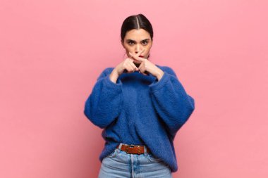 Genç ve güzel bir kadın ciddi ve hoşnutsuz görünüyor. İki parmağın önde olsun, reddedilmek için, sessizlik istiyor.