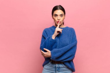Genç ve güzel bir kadın ciddi görünüyor ve parmaklarını dudaklarına bastırıp sessizlik ya da sessizlik talep ediyor, sır saklıyor.