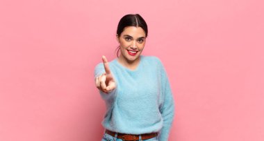 Genç ve güzel bir kadın gülümsüyor ve arkadaş canlısı görünüyor. Bir numarayı gösteriyor veya ilk eli önde, geriye doğru sayıyor.