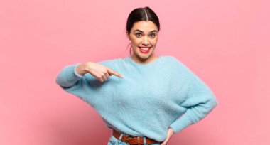 Genç, güzel bir kadın mutlu, gururlu ve şaşırmış görünüyor, neşeli bir şekilde kendini gösteriyor, kendinden emin ve kibirli hissediyor.