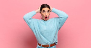Genç ve güzel bir kadın heyecanlı ve şaşırmış görünüyor, ağzı açık, iki eli de başında, kendini şanslı bir kazanan gibi hissediyor.