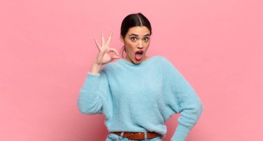 Genç ve güzel bir kadın kendini başarılı ve tatmin olmuş hissediyor, ağzı açık gülümsüyor, elle işaret veriyor.