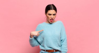 Genç ve güzel bir kadın şok olmuş ve şaşırmış görünüyor, ağzı açık, kendini işaret ediyor.