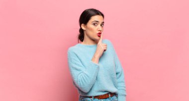 Genç ve güzel bir kadın sessizlik ve sessizlik istiyor, parmaklarıyla ağzının önünde işaret ediyor, 