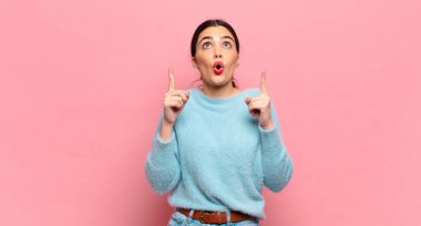 Genç ve güzel bir kadın huşu içinde ve ağzı açık bir şekilde şaşkın ve şaşkın bir bakışla yukarıya bakıyor.