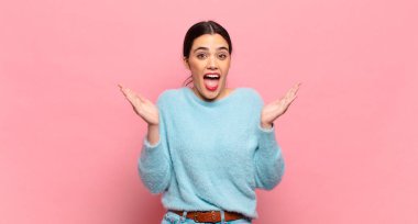Genç, güzel bir kadın mutlu ve heyecanlı görünüyor. Beklenmedik bir sürprizle şoke olmuş. İki eli yüzü açık.