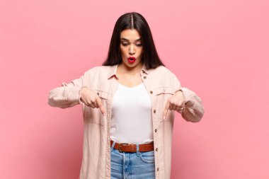 Genç, güzel bir kadın şoke olmuş, ağzı açık ve şaşırmış, inançsızlık ve şaşkınlık içinde bakıyor ve onu işaret ediyor.