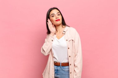 Genç ve güzel bir kadın ciddi ve meraklı görünüyor, dinliyor, gizli bir konuşma veya dedikodu duymaya çalışıyor, kulak misafiri oluyor.