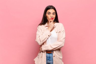 Genç ve güzel bir kadın ciddi, düşünceli ve güvensiz görünüyor. Bir kolu çapraz, eli çenesinde, seçenekleri değerlendiriyor.