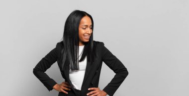 young black woman looking happy, cheerful and confident, smiling proudly and looking to side with both hands on hips. business concept