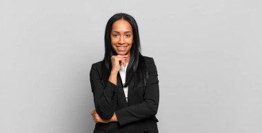 young black woman looking happy and smiling with hand on chin, wondering or asking a question, comparing options. business concept
