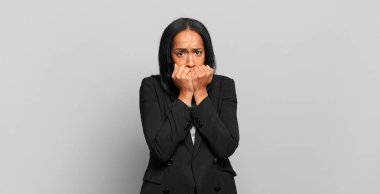 young black woman looking worried, anxious, stressed and afraid, biting fingernails and looking to lateral copy space. business concept