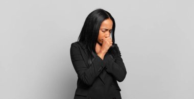 young black woman feeling ill with a sore throat and flu symptoms, coughing with mouth covered. business concept