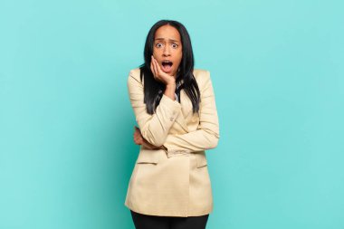 young black woman open-mouthed in shock and disbelief, with hand on cheek and arm crossed, feeling stupefied and amazed. business concept