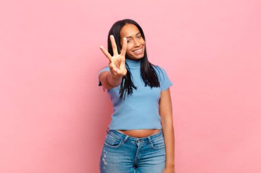 Genç siyahi kadın gülümsüyor ve arkadaş canlısı görünüyor. Elleri önde ve geriye doğru sayıyor.