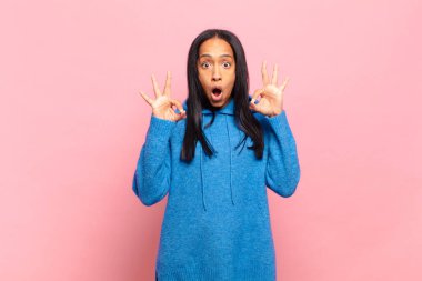 Genç siyahi kadın şok olmuş, şaşırmış ve şaşırmış hissediyor. Onaylıyor. İki eliyle de onay işareti yapıyor.