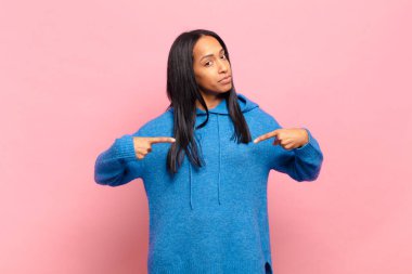 Genç siyah kadın gururlu, pozitif ve rahat görünüyor. İki eliyle göğsünü gösteriyor.