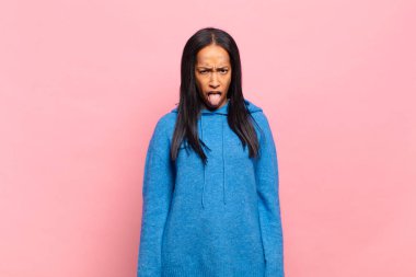 Genç siyahi kadın tiksinmiş ve rahatsız olmuş hissediyor. Dilini dışarı çıkarıyor. İğrenç ve iğrenç bir şeyden hoşlanmıyor.