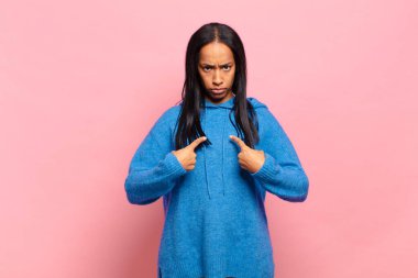 Genç siyahi kadın, şaşkın ve şaşkın bir bakışla kendini işaret ediyor. Seçildiğine şaşırmış ve şaşırmış.