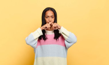 Genç siyahi kadın ciddi ve hoşnutsuz görünüyor. İki parmağının önde olması reddedilerek sessizlik istiyor.