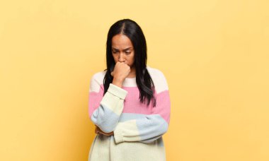 Genç siyahi kadın ciddi, düşünceli ve endişeli, elleri çenesine bastırılmış şekilde yan bakıyor.