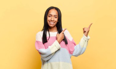 Genç siyahi kadın mutlu bir şekilde gülümsüyor ve her iki elini de fotokopi alanında objeler gösteriyor.