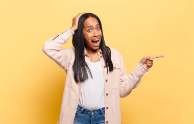 Genç siyahi kadın gülüyor, mutlu, pozitif ve şaşırmış görünüyor. Yan fotokopi alanını işaret eden harika bir fikrin farkına varıyor.