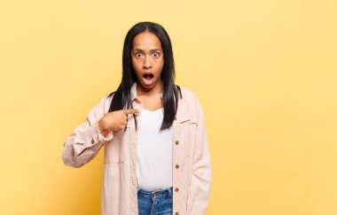 Genç siyahi kadın şok olmuş ve şaşırmış görünüyor, ağzı açık, kendini işaret ediyor.
