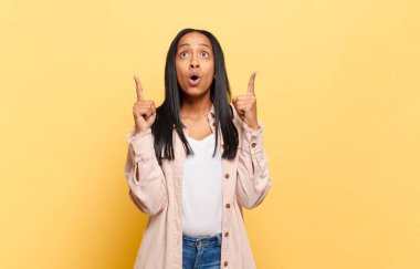 Genç siyahi kadın şaşkınlık ve ağzı açık bir şekilde şaşkın ve şaşkın bir bakışla yukarıya bakıyor.