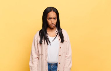 Genç siyahi kadın şaşkın ve şaşkın görünüyor. Sinirli bir hareketle dudağını ısırıyor. Sorunun cevabını bilmiyor.