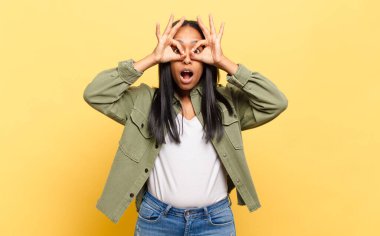 young black woman feeling shocked, amazed and surprised, holding glasses with astonished, disbelieving look