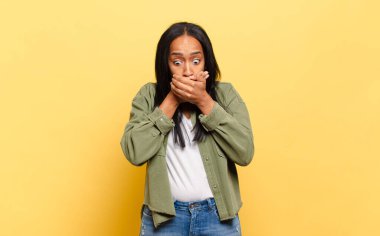 young black woman covering mouth with hands with a shocked, surprised expression, keeping a secret or saying oops
