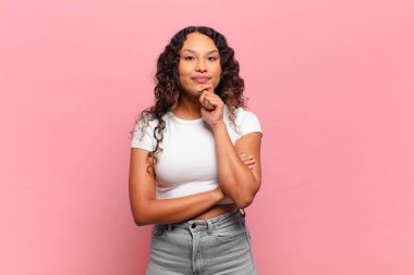 Genç İspanyol kadın mutlu, kendinden emin bir ifadeyle gülümsüyor, çenesinde elleri, merak ediyor ve yan tarafa bakıyor.