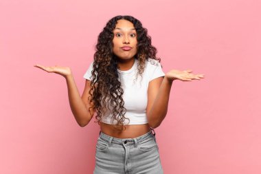 Genç İspanyol kadın şaşkın, şaşkın ve stresli görünüyor, farklı seçenekler arasında merak ediyor, kararsız hissediyor.