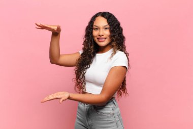 Genç İspanyol kadın gülümsüyor, mutlu, pozitif ve memnun, fotokopi alanında nesne ya da konsept tutuyor ya da gösteriyor