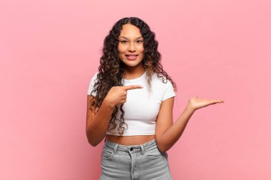 Genç İspanyol kadın gülümsüyor, mutlu, kaygısız ve tatmin olmuş hissediyor, fotokopi alanındaki konsepte ya da fikre işaret ediyor.